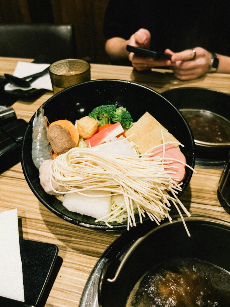 A vibrant Asian hotpot bowl with fresh vegetables and noodles on a restaurant table.