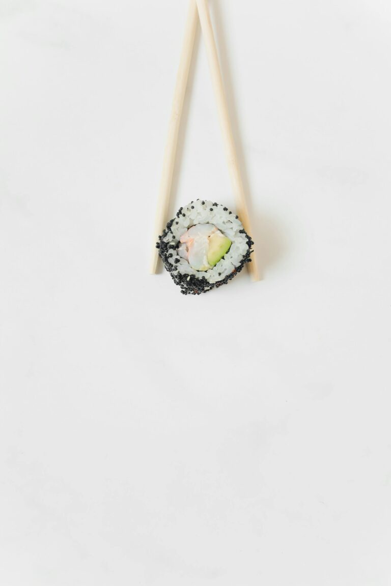 A single sushi roll with chopsticks on a clean white surface, showcasing modern food presentation.